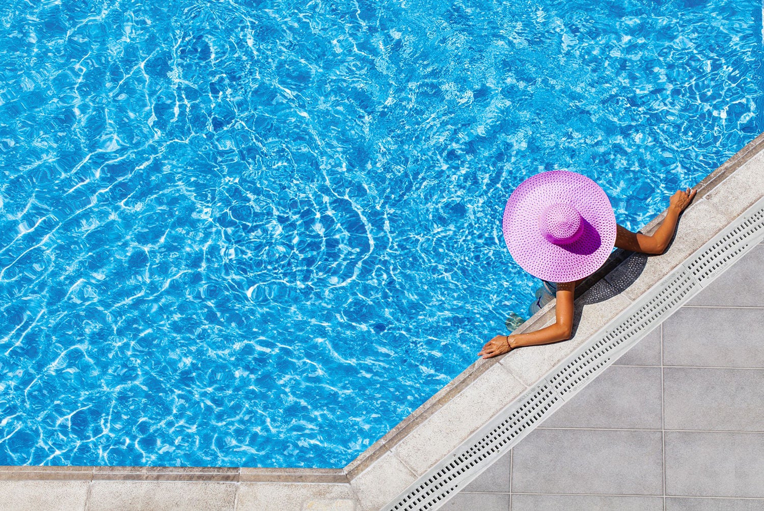 woman lounging at the pool next to channel drain in pink hat